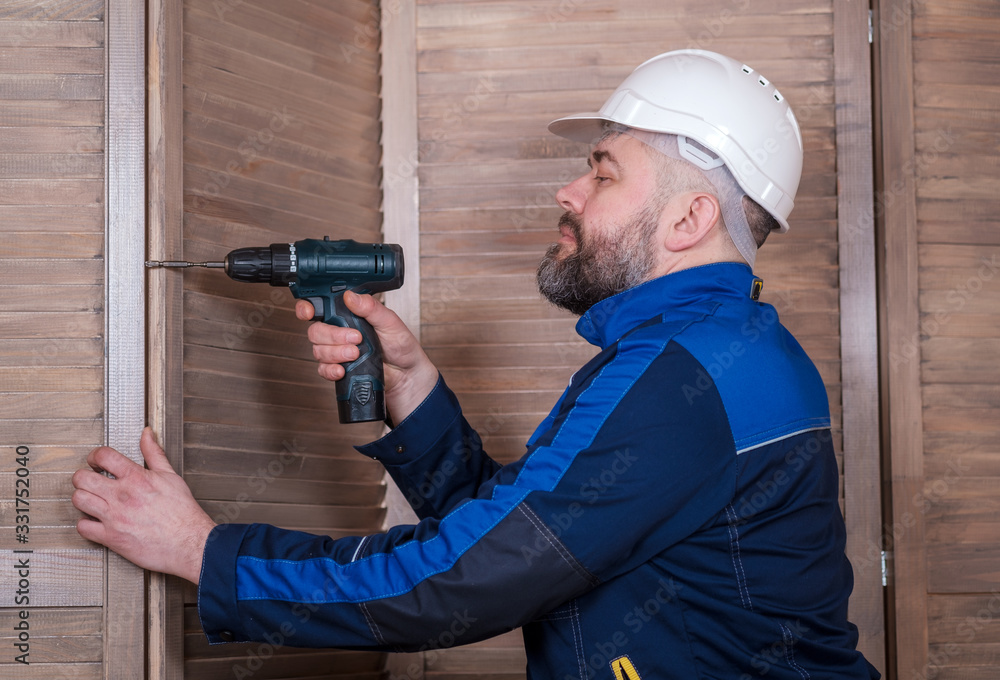 a bearded man carpenter with a screwdriver in his hands is assembling wooden louver panels a bearded man carpenter with a screwdriver in his hands is assembling wooden louver panels