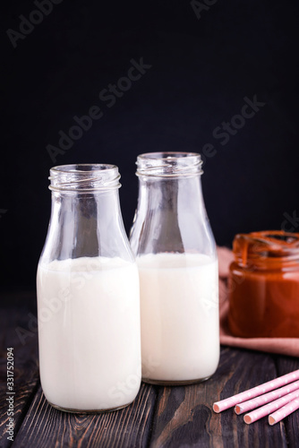 Two bottles of fresh milk with tubes and fresh homemade salted caramel n dark background.