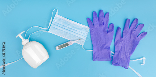 Photography Top view of protective face mask, medical gloves, thermometer and hand gel on blue background