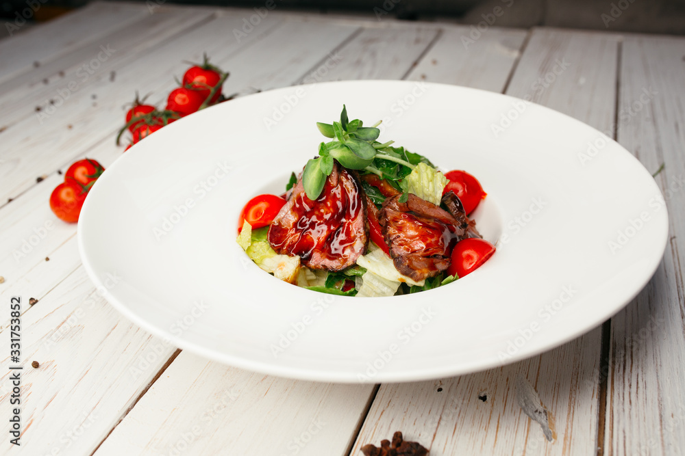 Vegetable salad with meat and barbecue sauce served on a large round white plate. Restaurant dish on a wooden background. Vegetable salad with meat and barbecue sauce served on a large round white plate. Restaurant dish on a wooden background.