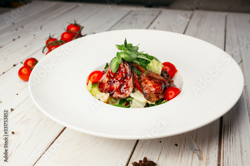 Vegetable salad with meat and barbecue sauce served on a large round white plate. Restaurant dish on a wooden background.