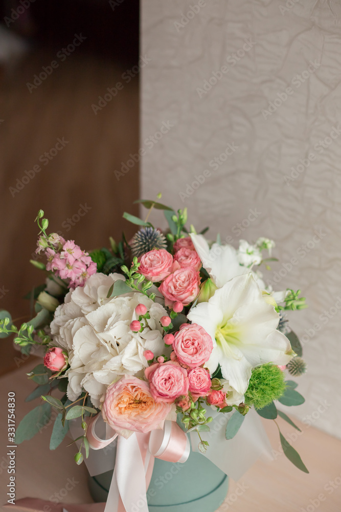 A large flower arrangement in a hat box was created by a florist for a wedding gift. Hydrangea, amarallis, roses and eucalyptus in a bouquet