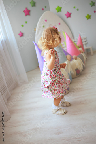 cute little Caucasian girl in floral print dress playing with big dwarf dolls in her room