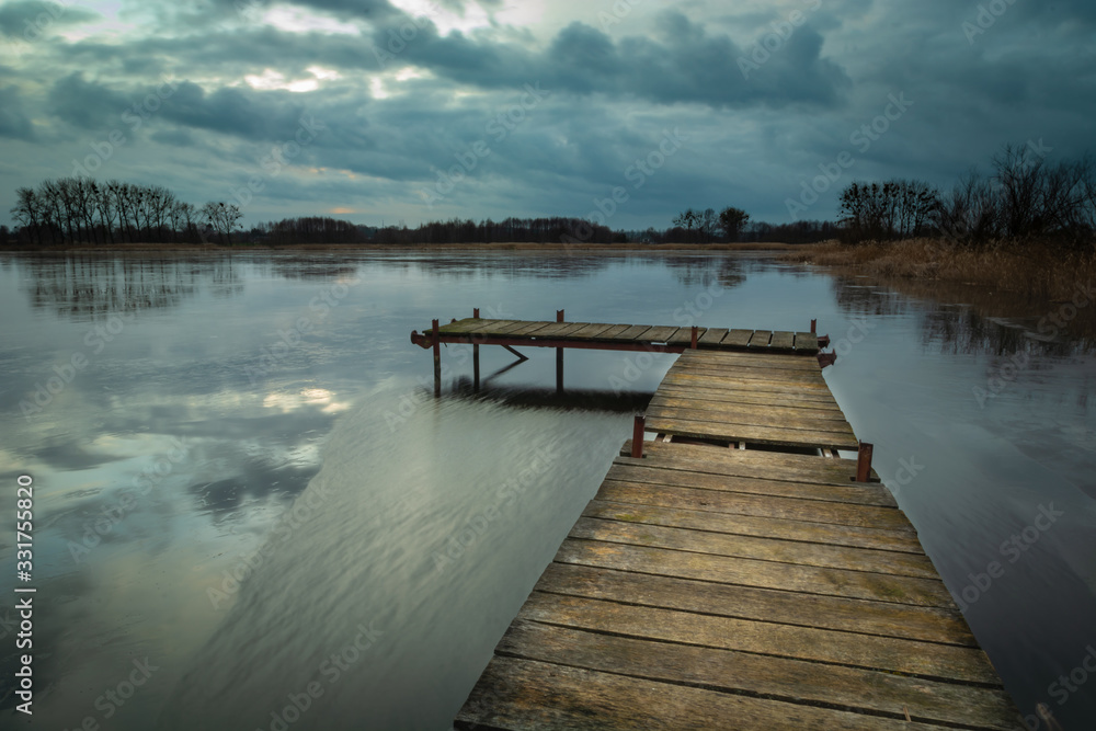 Wooden jetty on a lake and dark clouds on sky Wooden jetty on a lake and dark clouds on sky