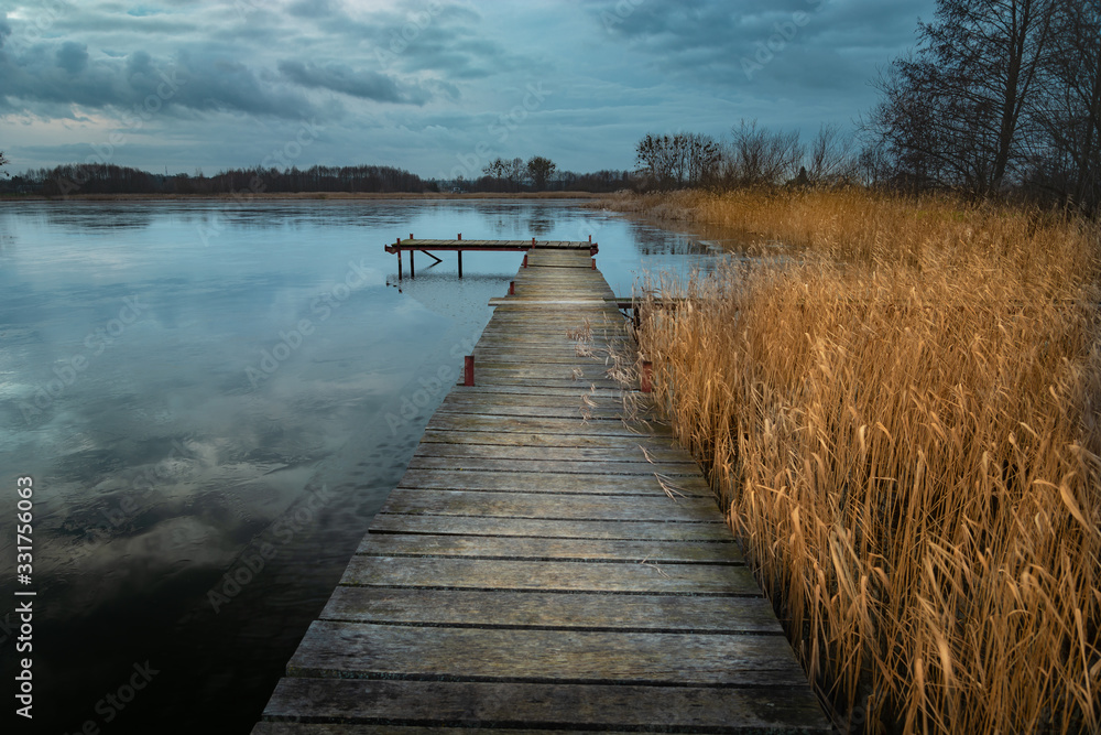 A long wooden bridge and reed on the lake, dark clouds on the sky