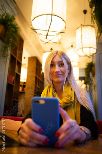 woman looks at a smartphone in a cafe in the light of artificial cafe lamps photo