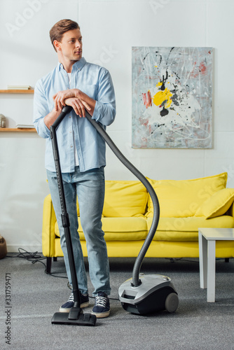Handsome man standing near vacuum cleaner in living room