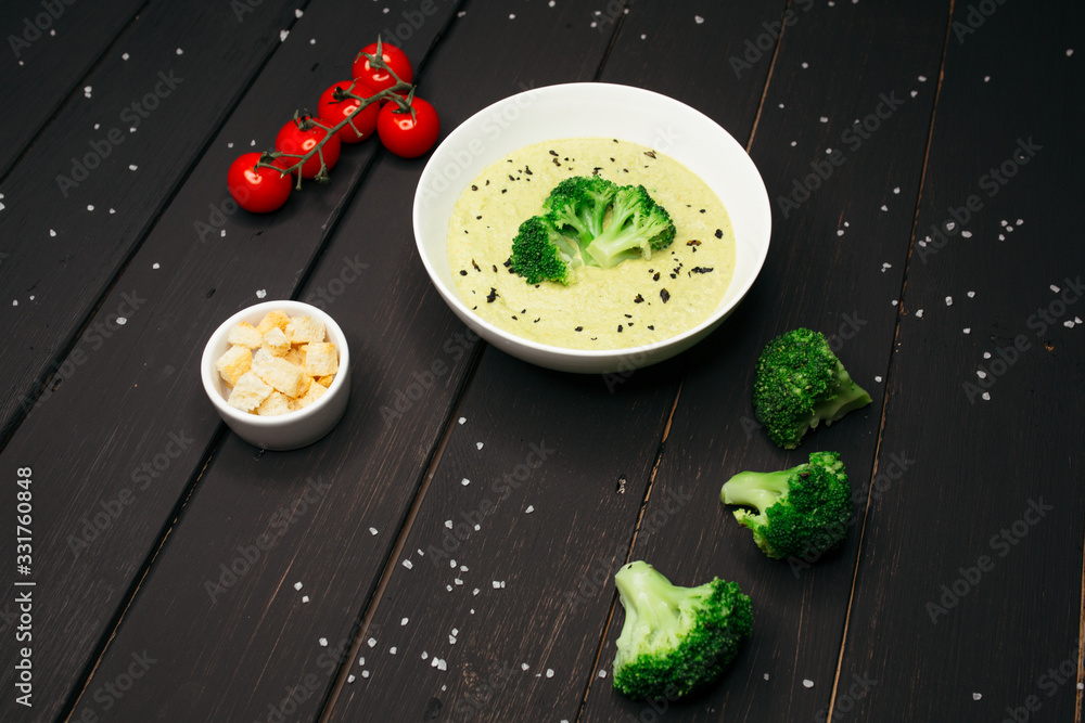 Delicate broccoli cream soup served on a dark white plate on a black wooden table sprinkled with sea salt.