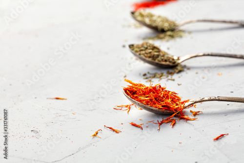 Saffron seasoning in an old silver spoon on the background of other seasonings in blur on a gray concrete background.