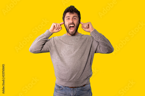 Young handsome man wearing casual sweater standing over isolated yellow background angry and mad screaming frustrated and furious, shouting with anger. Rage and aggressive concept.