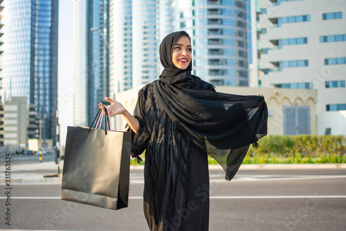 Beautiful middle eastern woman in abaya holding shopping bags on city street photo