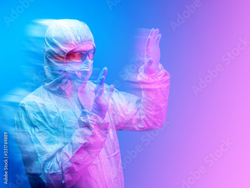 A chemist in a protective suit , mask and yellow glasses on a blue background in a protective pose.