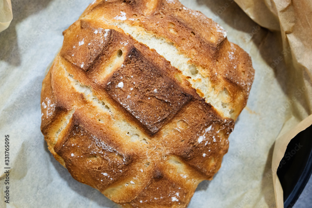Close up on fresh baked homemade traditional rustic loaf of bread in the casserole dish over baking paper top view Close up on fresh baked homemade traditional rustic loaf of bread in the casserole dish over baking paper top view