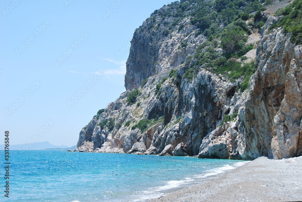 Wild beach on the Mediterranean coast. Empty pebbles beach, turquoise sea and rocks.