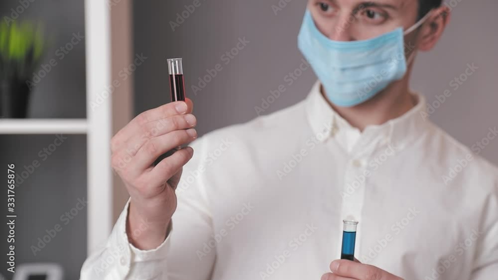 Close up laboratory doctor holds two test tubes of red and blue colors and examines them. The doctor examines the laboratory test tubes. Close up laboratory doctor holds two test tubes of red and blue colors and examines them. The doctor examines the laboratory test tubes.