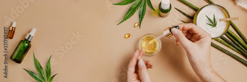 Pipette with CBD cosmetic oil in female hands on a table background with cosmetics, cream with cannabis and hemp leaves, marijuana