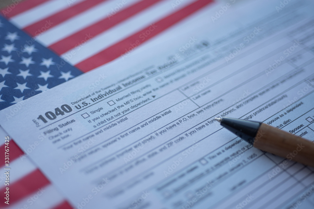 Obraz premium Form 1040 U.S. Individual Income Tax return next to flag of USA. Close up view.