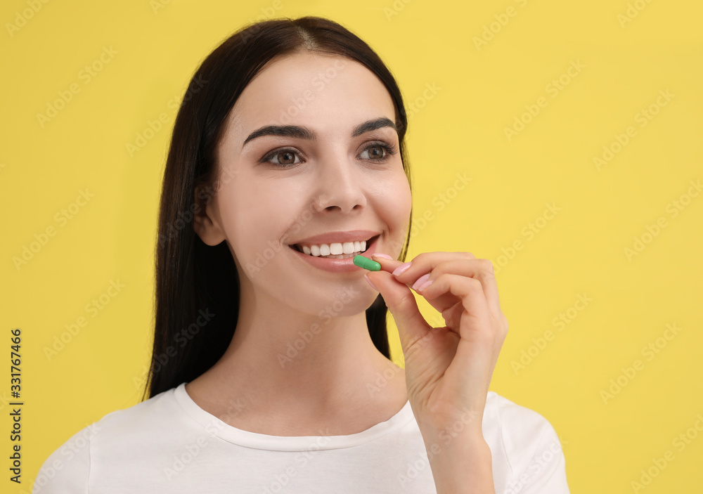 Young woman taking vitamin capsule on yellow background Young woman taking vitamin capsule on yellow background