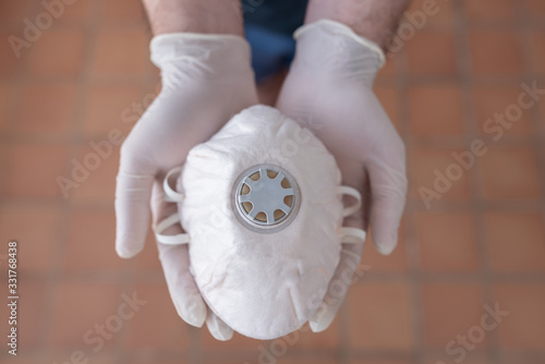  Close up of hands with a medical face mask for protection. Two hands with white esterilized gloves holding a medical mask. Protection against CORONAVIRUS, diseases, infections and viruses. COVID-2019 photo