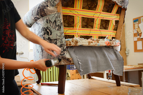 Making new upholstery on old restored furniture. Woman work with pneumatic stapler in upholstery workshop. Restoration of old armchair.