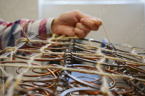 Upholstery springs. Upholstery worker tying old srpings. Upholstery workshop. Old chair springs restoration. Woman working. Hand and string.