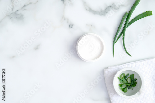 Cosmetic cream jar and green sliced stems aloe vera on marble background. Organic moisturizer hand cream. Hand skin care and beauty treatment concept