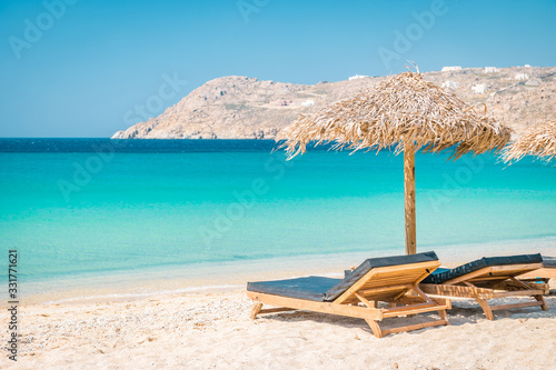 Fototapeta Naklejka Na Ścianę i Meble -  Mykonos beach during summer with umbrella and luxury beach chairs beds, blue ocean with mountain at Elia beach Mikonos Greece