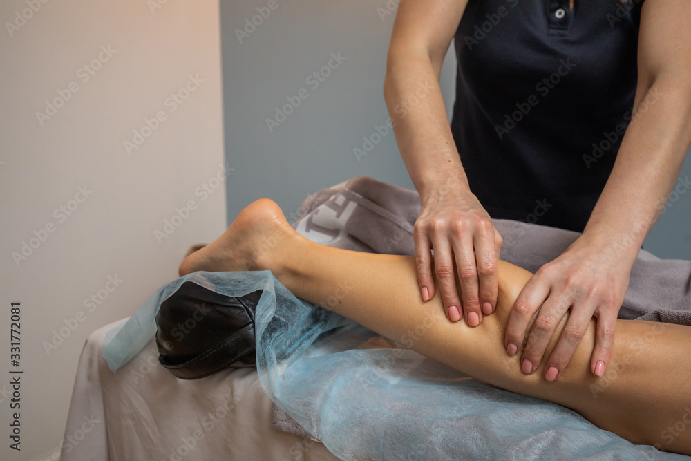 Hands of Female Masseur Master Makes Relaxing Leg Massage For Young Woman Close Up. The Masseur Kneads The Calf Muscle Of The Client