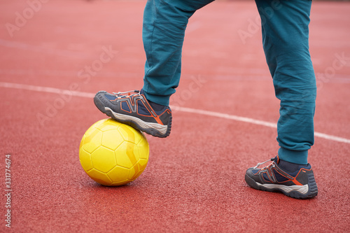 Boy holding a ball with his foot on a school playground  legs close