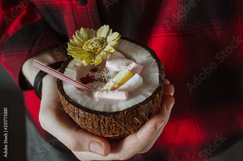 Female hand holding a coconut cocktail with berries and flower