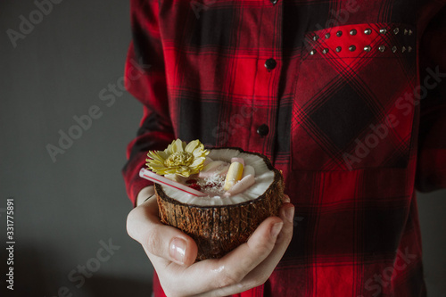 Female hand holding a coconut cocktail with berries and flower