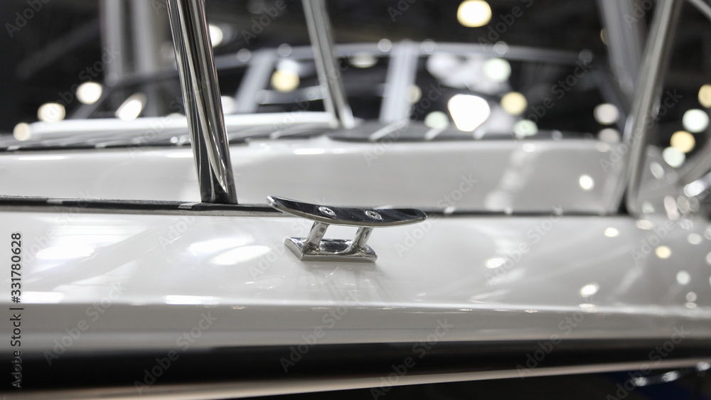 Shiny stainless mooring cleat on white motor boat deck close up, marine equipment