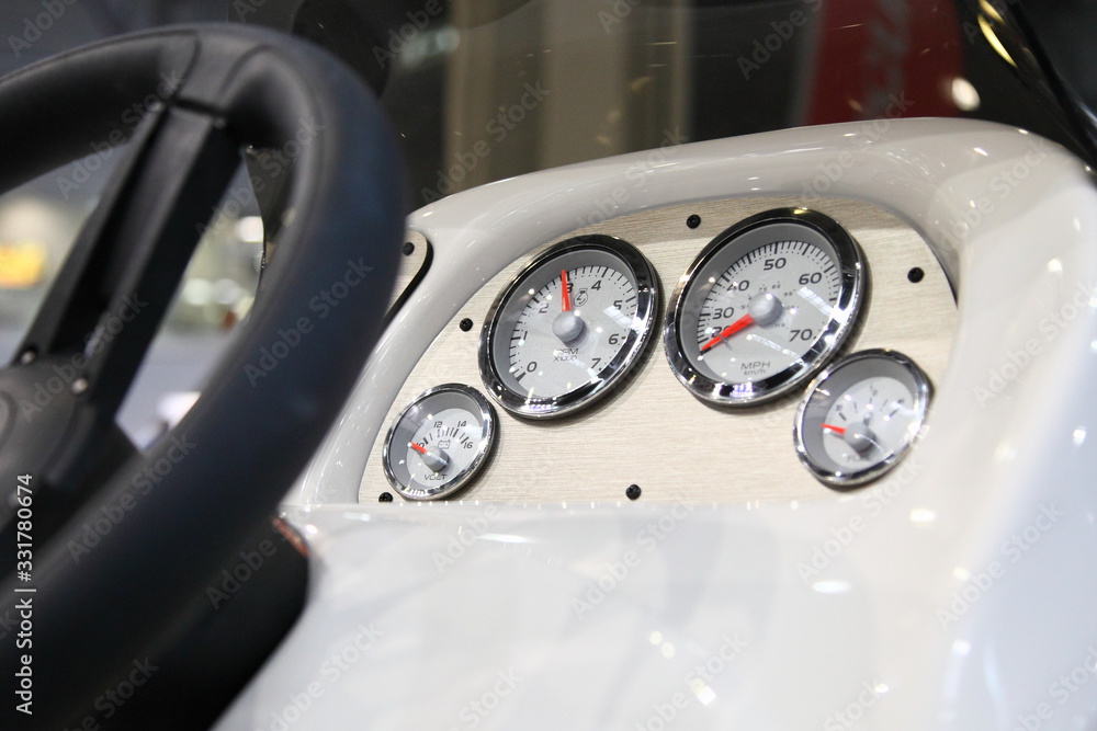 Modern motor boat telemetry devices, marine white analog appliances on dashboard in cockpit on blurred steering wheel background - speedometer, tachometer, voltage control and fuel meter
