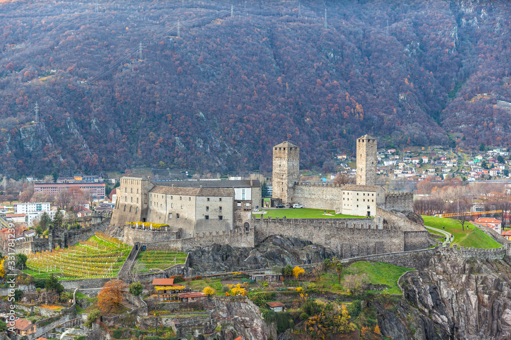 Aerial close up view of Castelgrande Castle ruin located on a hill from Montebello Castle in autumn, with colourful trees and green grass, Bellinzona, Ticino, Switzerland