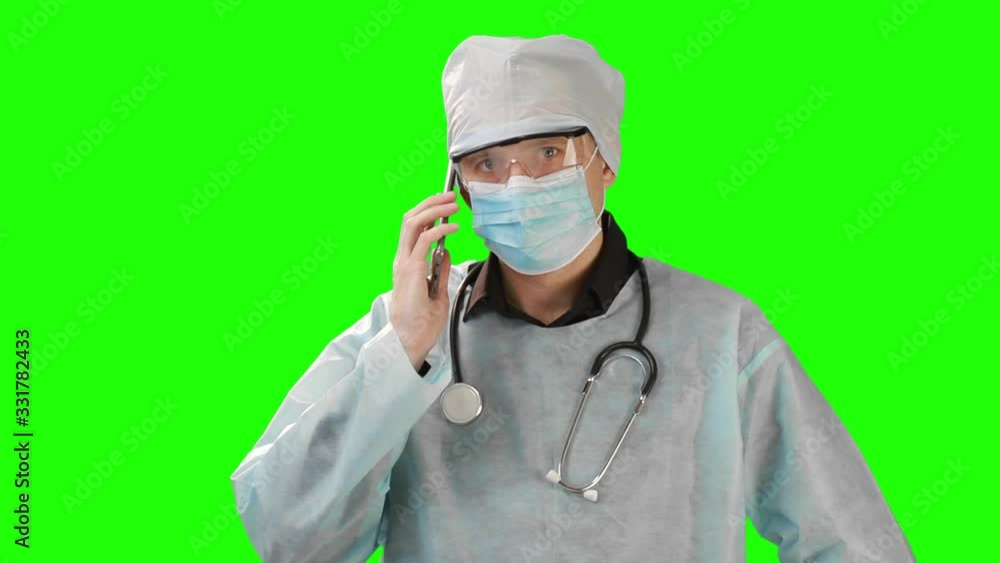Young doctor in medical mask and protective medical clothing talking on the phone. Shot on the background of Chrome Key. Chrome Kay high quality Young doctor in medical mask and protective medical clothing talking on the phone. Shot on the background of Chrome Key. Chrome Kay high quality