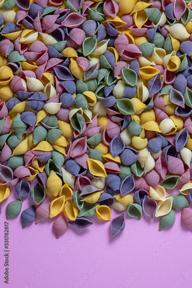 Fototapeta premium Pasta Conchiglie Rigate, mix of colorful uncooked shells with spinach and tomatoes. Textured Italian food background concept. Top view flat lay close up copy space