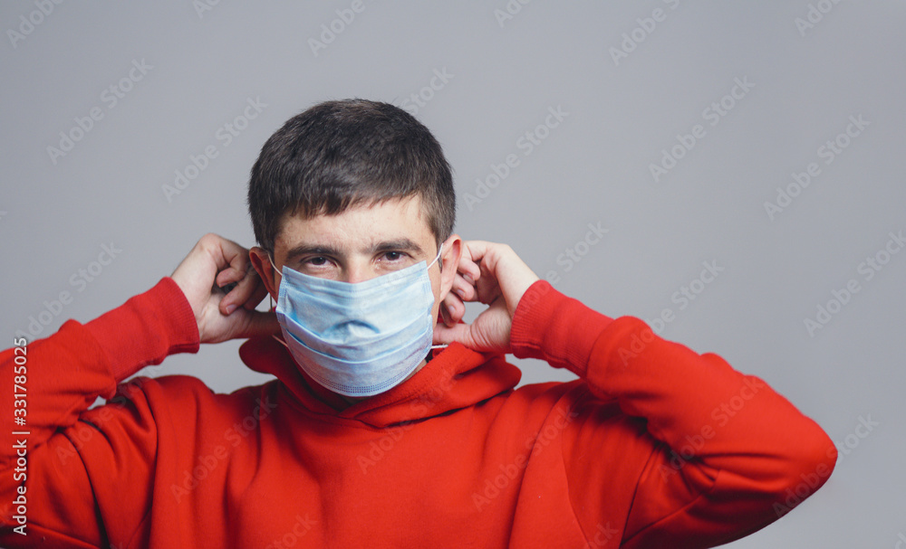 Portrait of young man putting medical flu mask on face, on gray studio background, quarantine measures and life saving concept Portrait of young man putting medical flu mask on face, on gray studio background, quarantine measures and life saving concept