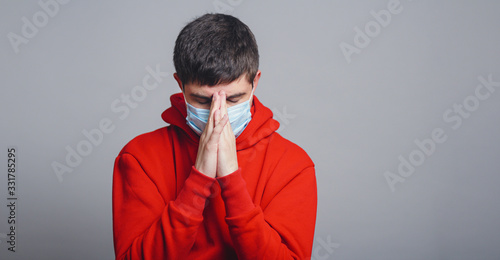young man in a protective medical mask on his face bowed his head in sorrow on a gray studio background, concept of health and global epidemic disease,man pray and asks for God's help