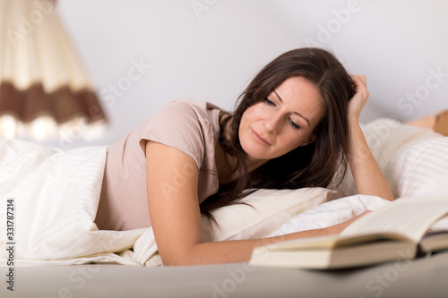 Frau träumt mit geschlossenen Augen im Bett und liest ein Buch
