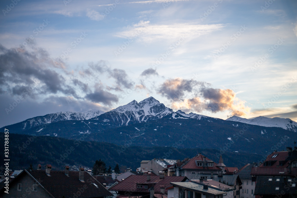 Alpine mountains with snowy peaks. Old european houses. Blue sky with clouds.