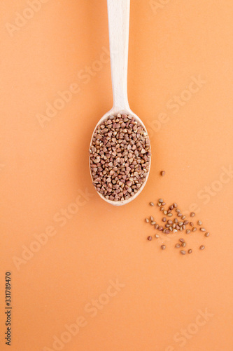 Raw buckwheat in the wooden spoon on the light brown background. Location vertical. Top view. Copy space.