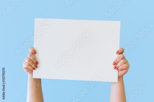 Close up cropped hold in hands blank empty sign white big board for promotional content, pointing finger on place for text isolated on blue background in studio. Copy space advertising area mock up