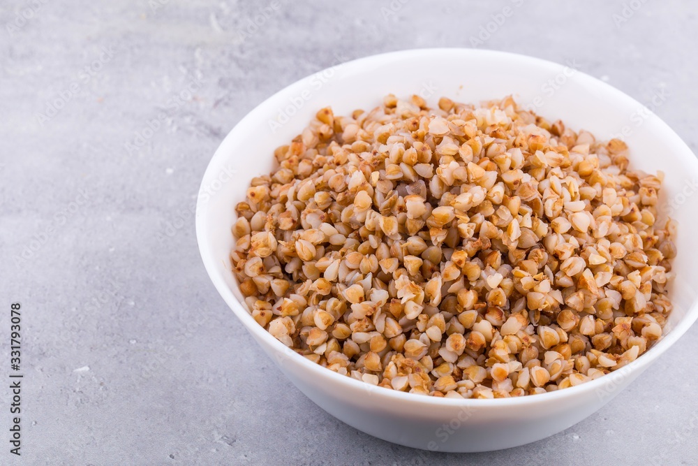 Cooked buckwheat in white ceramic bowl on grey background. Top view, horizontal format. Cooked buckwheat in white ceramic bowl on grey background. Top view, horizontal format.