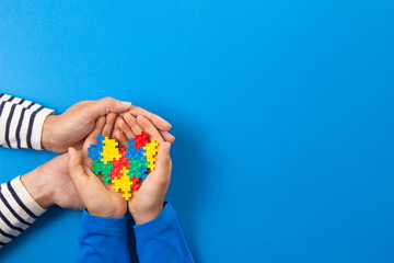 World autism awareness day concept. Adult and child hands holding puzzle heart on light blue background