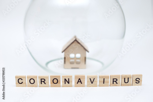 Model of a wooden house under a glass dome and wooden letters with the inscription Coronavirus ...