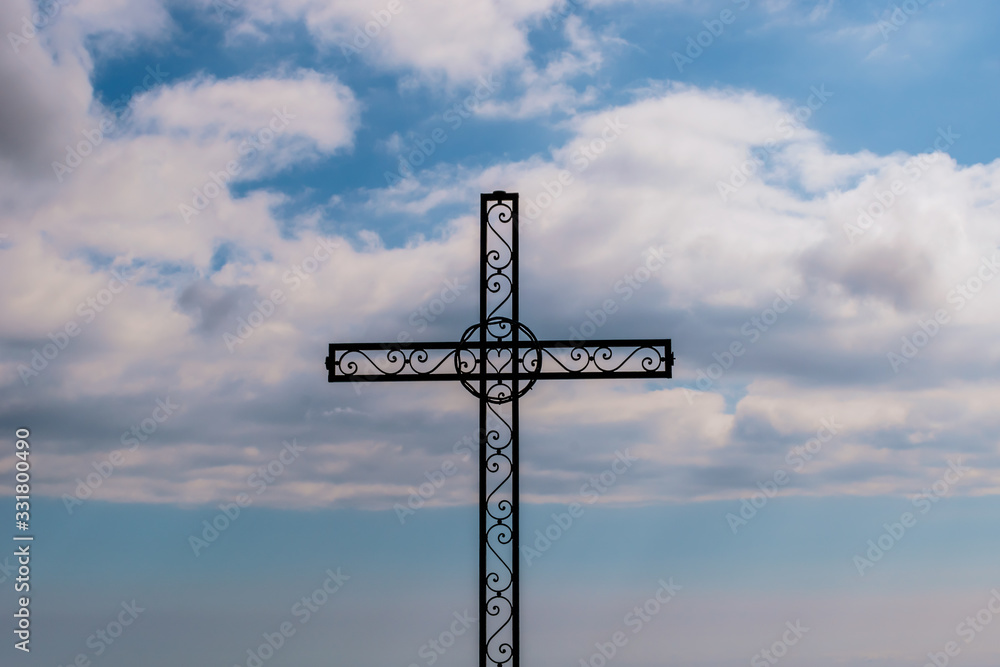 A close-up of a metal cross on top of a cliff Baou des Noirs near Vence, France in the Alps mountains with blue cloudy sky in the background (Cote d'Azur / Provence)