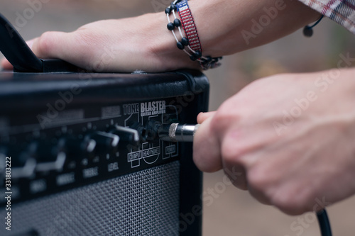 Hand inserts a cord jack into a combo amplifier for electric guitar
