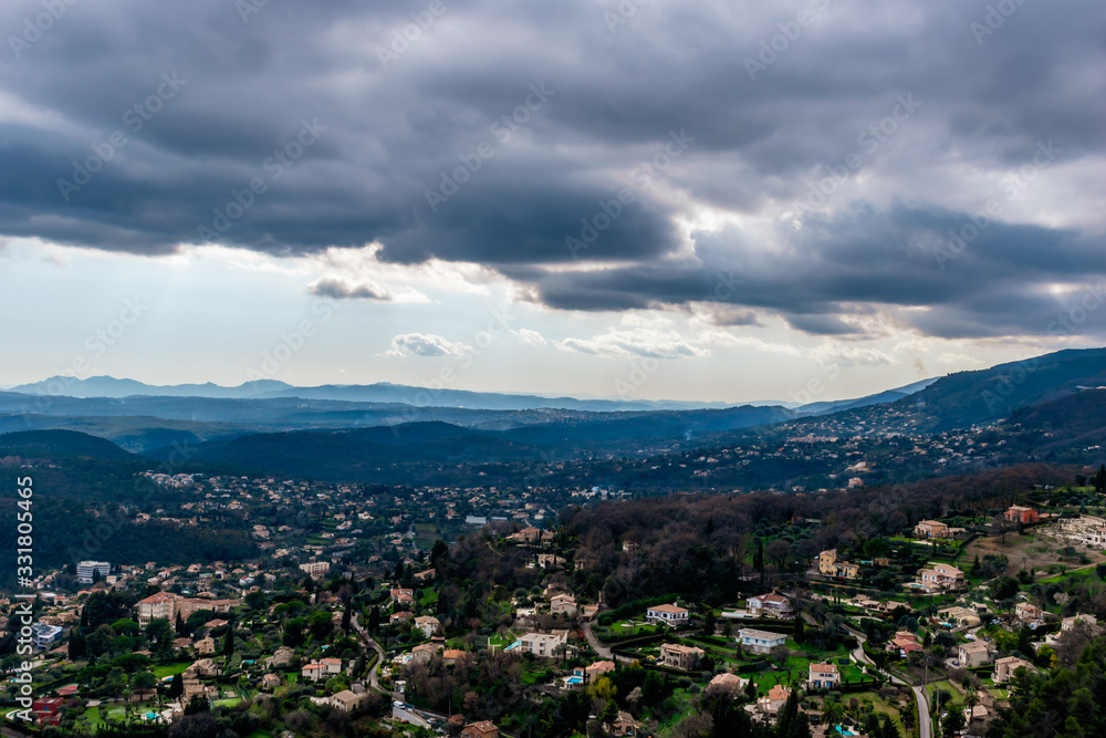 A wide / high angle panoramic view of houses and other buildings of several towns covering the low Alps mountains hills with the mountain ranges in the haze (French Côte d'Azur/ Provence/ Riviera)