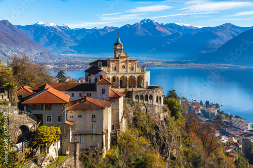Stunning close up panorama view of Madonna del Sasso church above Locarno city with Lake Maggiore, snow covered Swiss Alps mountain peak and blue sky cloud in background in autumn, Ticino, Switzerland photo