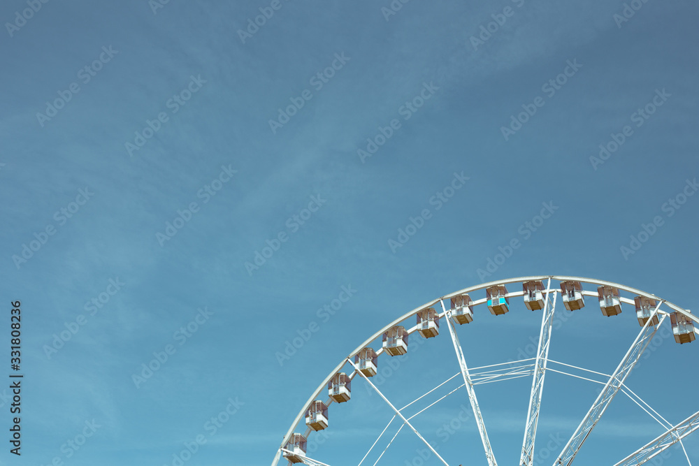 Beautiful ferris wheel with white cabs on a background of blue sky Beautiful ferris wheel with white cabs on a background of blue sky